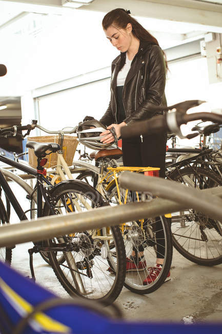 Belle femme tenant casque au stand de vélo — Photo de stock