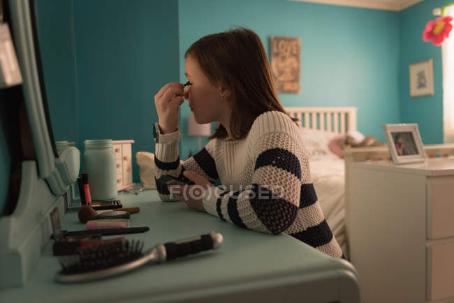 Chica aplicando delineador de ojos en el dormitorio en casa - foto de stock