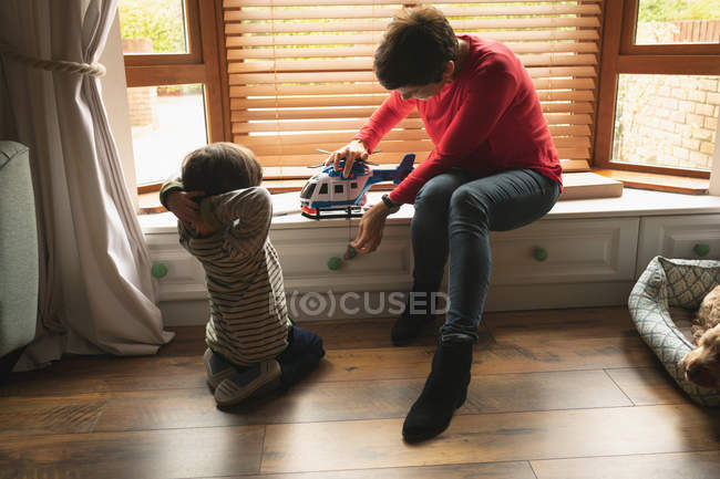 Madre jugando con su hijo en el asiento de la ventana en la sala de estar en casa - foto de stock