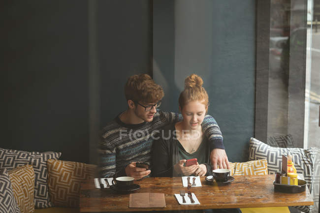 Pareja joven usando teléfonos móviles en la cafetería - foto de stock