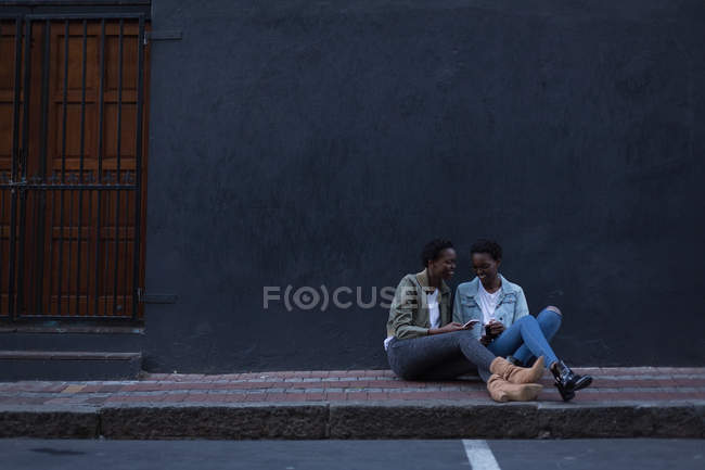 Gemelos hermanos usando el teléfono móvil en la acera en la calle de la ciudad - foto de stock