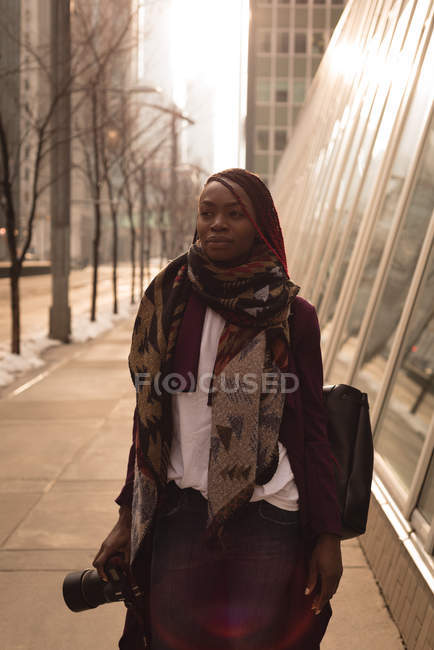 Femme réfléchie debout avec appareil photo numérique dans la ville — Photo de stock