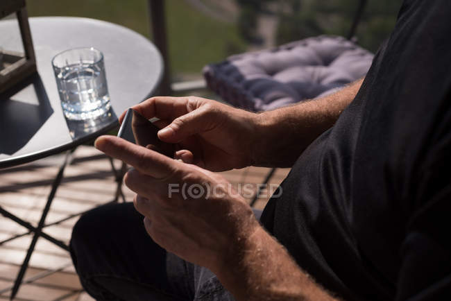 Sección media del hombre usando el teléfono móvil en la sala de estar en casa - foto de stock