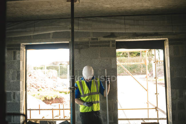 Ingeniero con medidor de nivel usando su teléfono en el sitio de construcción - foto de stock