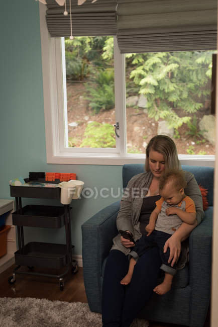 Mother and baby sitting on the sofa and using mobile at home — Stock Photo