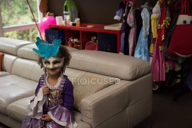 Girl wearing masquerade masks sitting on sofa at home — Stock Photo