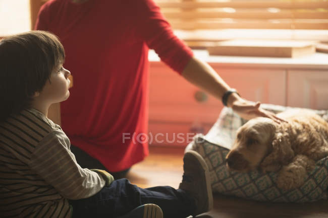 Madre e hijo acariciando perro en la sala de estar en casa - foto de stock