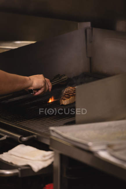 Male chef cooking meat in barbecue at kitchen — Stock Photo