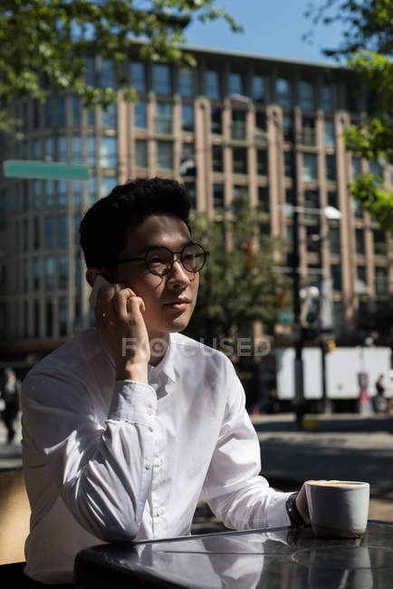 Junger Mann greift im Outdoor-Café zum Handy — Stockfoto