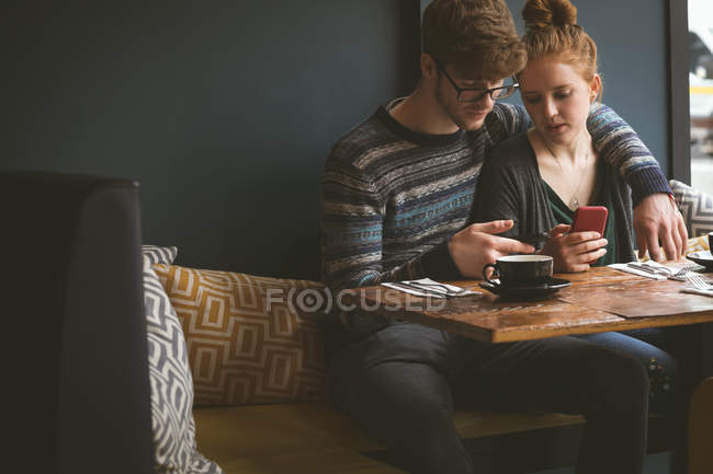 Jeune couple utilisant des téléphones mobiles dans le café — Photo de stock