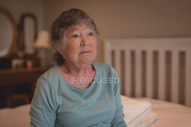 Preoccupata donna anziana seduta sul letto a casa — Foto stock