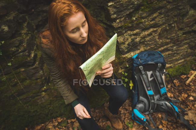Randonneuse rousse avec sac à dos lisant une carte dans la forêt — Photo de stock