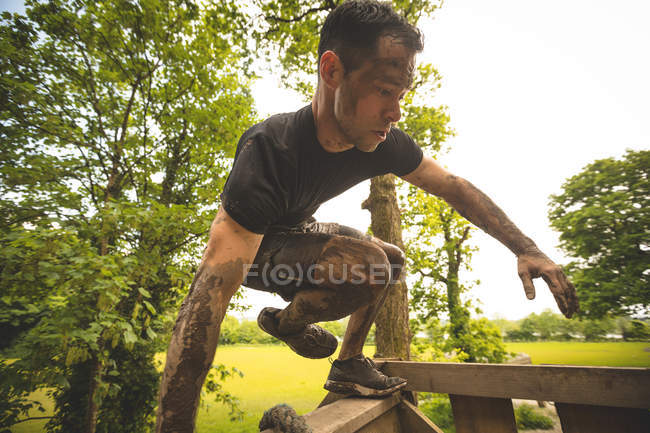 Entrenamiento de hombre adecuado sobre la carrera de obstáculos en el campo de entrenamiento - foto de stock
