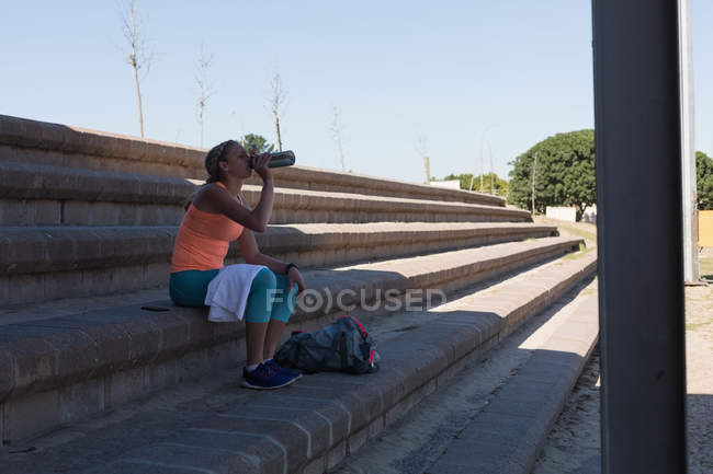 Female athlete drinking water at sports venue — Stock Photo
