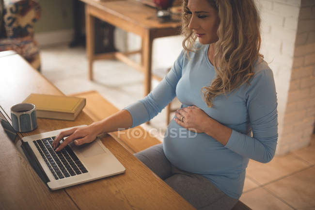Красива вагітна жінка використовує ноутбук вдома — стокове фото