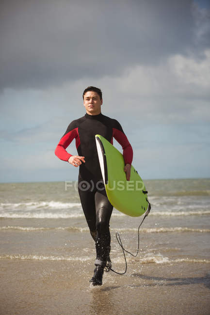 Surfista determinado con tabla de surf corriendo en la playa - foto de stock