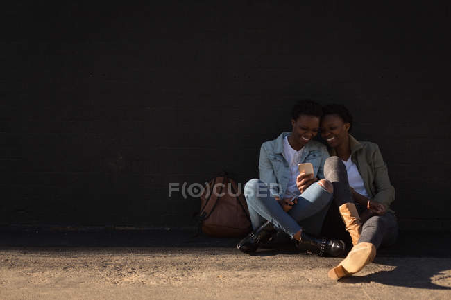 Hermanas gemelas felices usando teléfono móvil en la calle de la ciudad - foto de stock