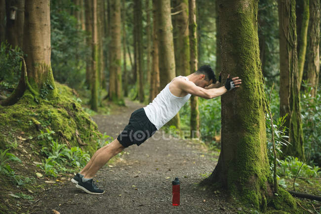 Fit man doing stretching exercise in forest — Stock Photo