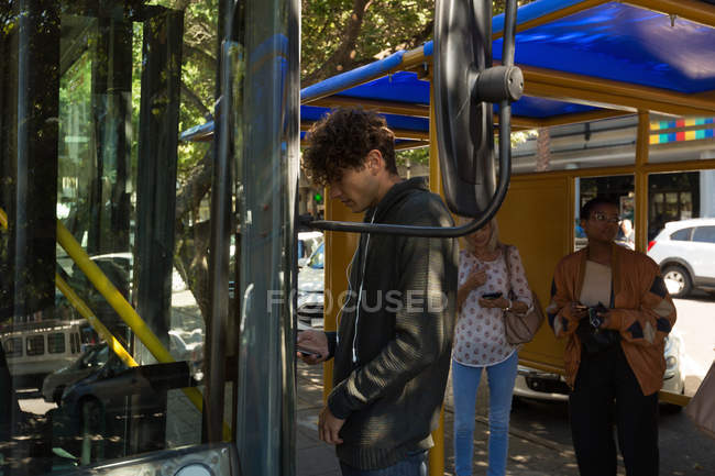 Giovane uomo imbarco autobus durante l'utilizzo del telefono cellulare — Foto stock