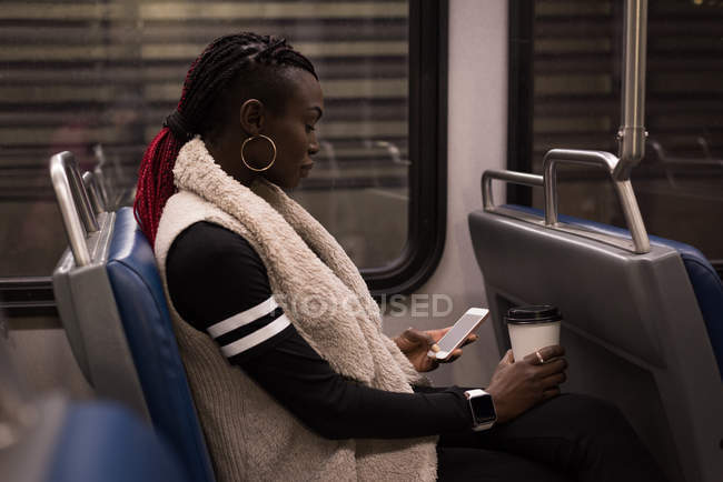 Mujer joven usando el teléfono móvil mientras viaja en tren - foto de stock
