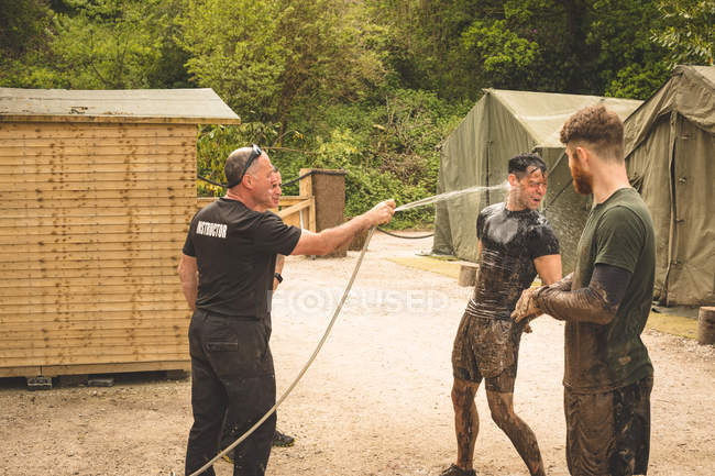 Trainer washing man's face with water at boot camp — Stock Photo