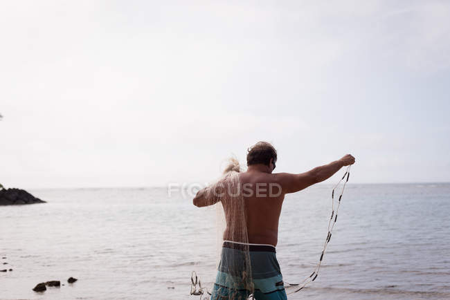 Fisherman holding fishing net on the beach — Stock Photo