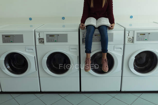Sección baja del libro de lectura de la mujer mientras espera en la lavandería - foto de stock