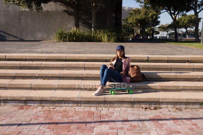 Жінка сидить на сходах і використовує мобільний телефон в парку — стокове фото