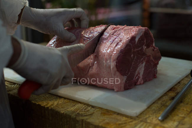 Mid section of butcher cutting meat at butcher shop — Stock Photo
