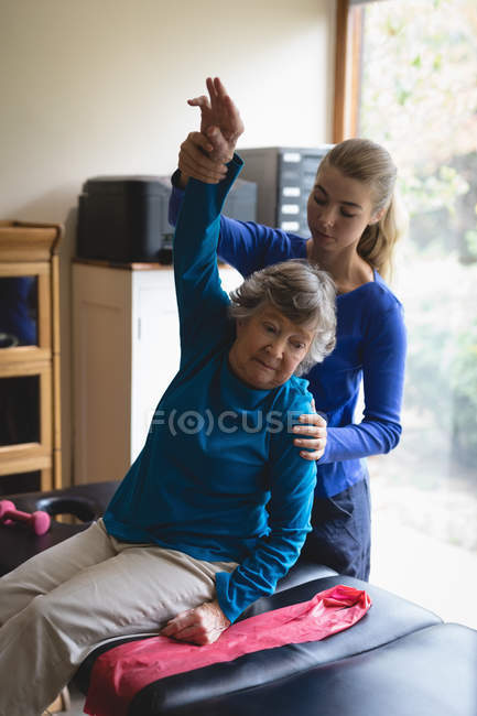 Fisioterapeuta asistiendo a una mujer mayor con ejercicios de fisioterapia en casa - foto de stock