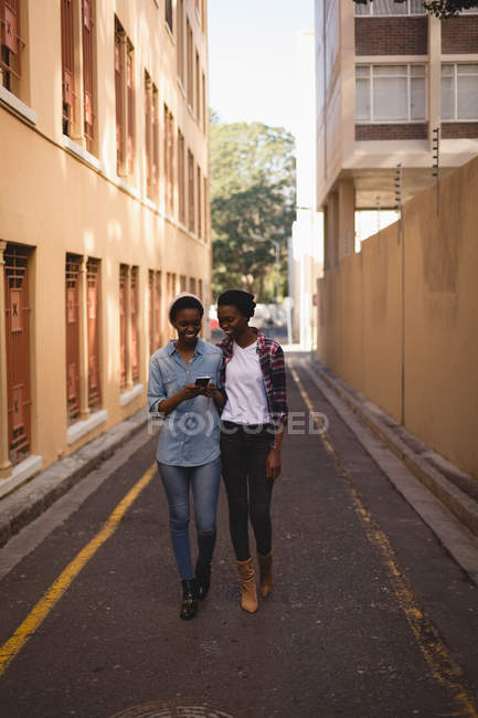 Gêmeos irmãos usando telefone celular enquanto caminham na rua em um dia ensolarado — Fotografia de Stock
