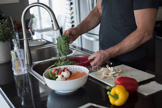 Homem lavando legumes na cozinha em casa — Fotografia de Stock