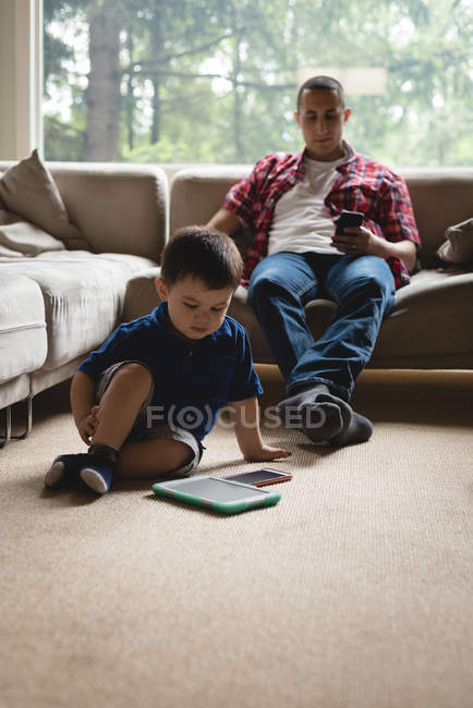 Pai e filho usando tablet digital e telefone celular na sala de estar em casa — Fotografia de Stock