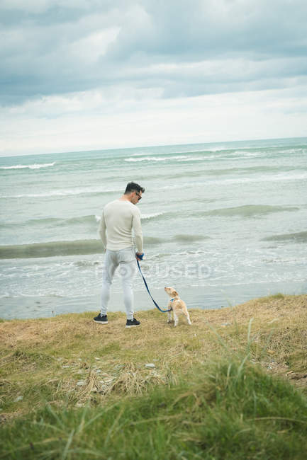 Вид ззаду чоловіка зі своїм собакою, що стоїть на березі моря — стокове фото
