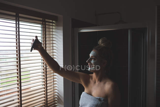 Жінка з кремом для обличчя бере селфі з мобільним телефоном у ванній вдома — стокове фото