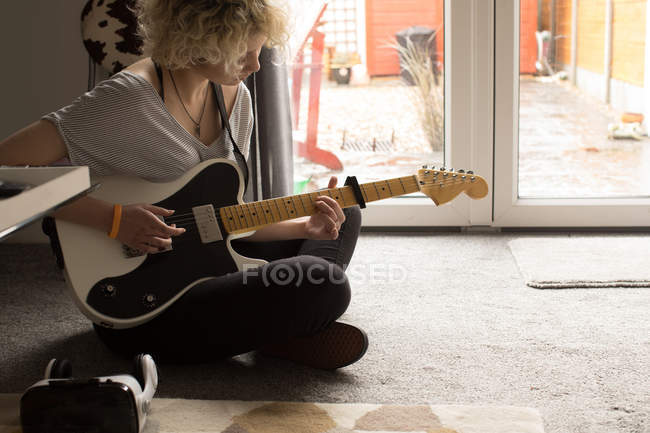 Молода жінка грає на гітарі у вітальні вдома — стокове фото