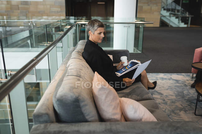 Businesswoman with coffee cup reading documents in the office — Stock Photo