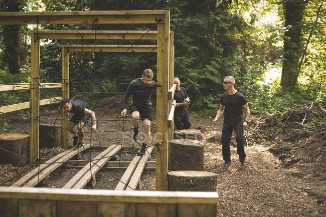 Grupo de entrenamiento de hombres en carrera de obstáculos en entrenamiento de campo de entrenamiento - foto de stock