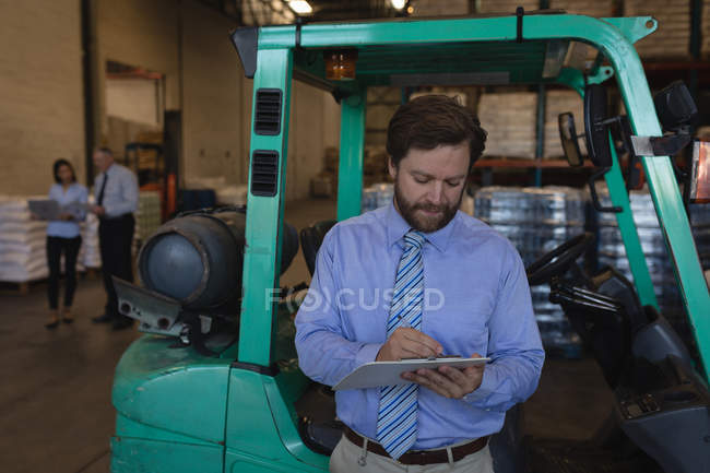 Superviseur masculin écrivant sur un presse-papiers dans l'entrepôt — Photo de stock