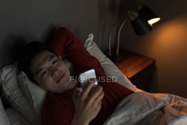 Человек, использующий мобильный телефон в спальне дома — стоковое фото
