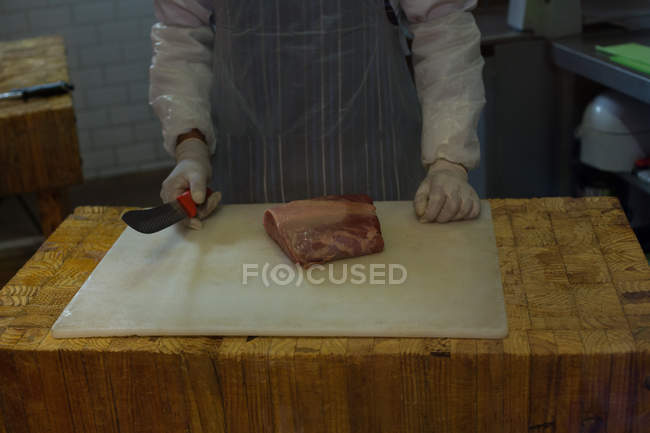 Corte médio de açougueiro de pé com pedaço de carne no açougue — Fotografia de Stock