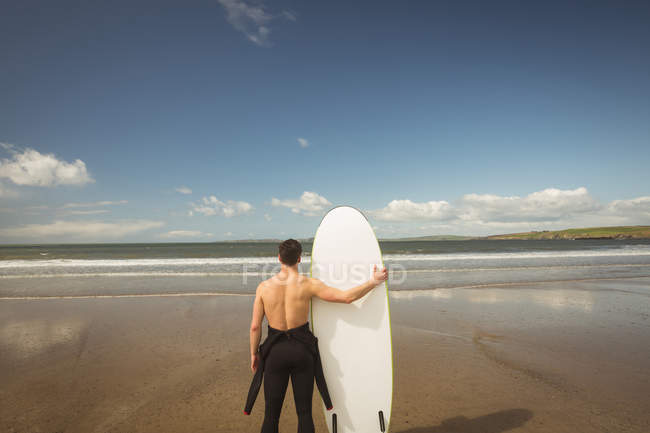 Rear view of surfer with surfboard looking at the sea from beach — Stock Photo