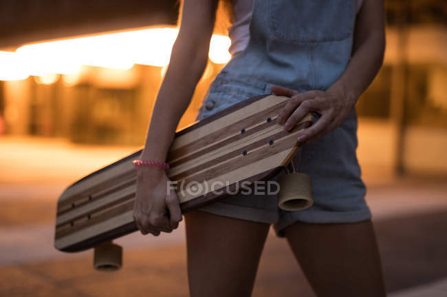 Средняя часть фигуристки держит скейтборд в городе — стоковое фото