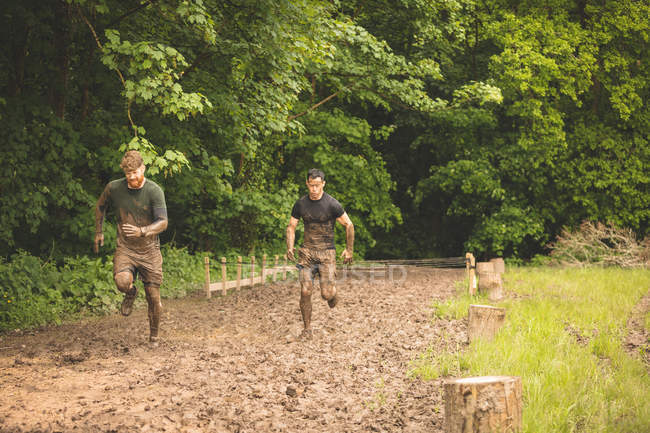 Ajuste los hombres que entrenan sobre carrera de obstáculos en el campo de entrenamiento - foto de stock