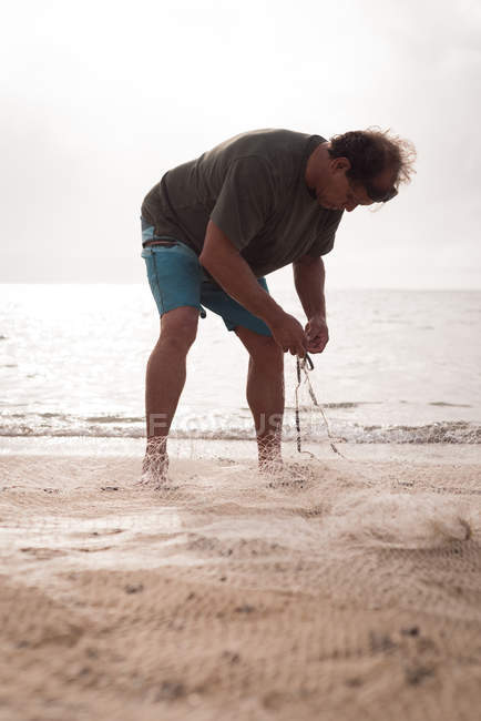 Зрілий рибалка тримає рибальську сітку на пляжі — стокове фото