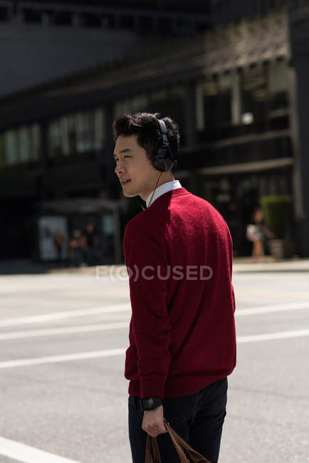 Молодий чоловік слухає музику на навушниках під час перетину вулиці — стокове фото