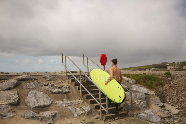 Surfista com prancha caminhando em direção ao mar em um dia ensolarado — Fotografia de Stock