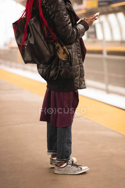 Sección baja de la mujer que utiliza el teléfono móvil en la plataforma ferroviaria - foto de stock