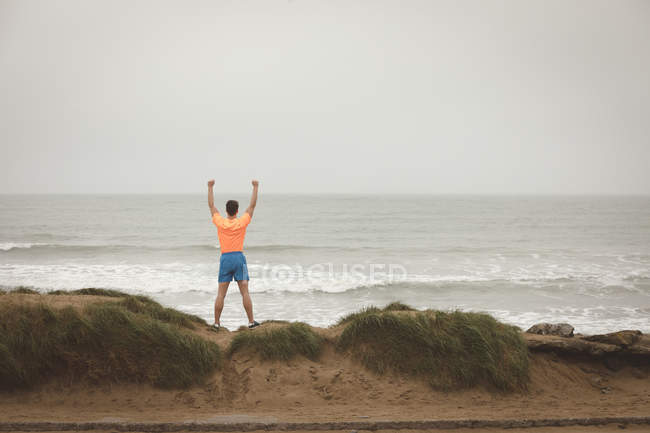 Visão traseira do homem de pé com as mãos levantadas na costa do mar — Fotografia de Stock