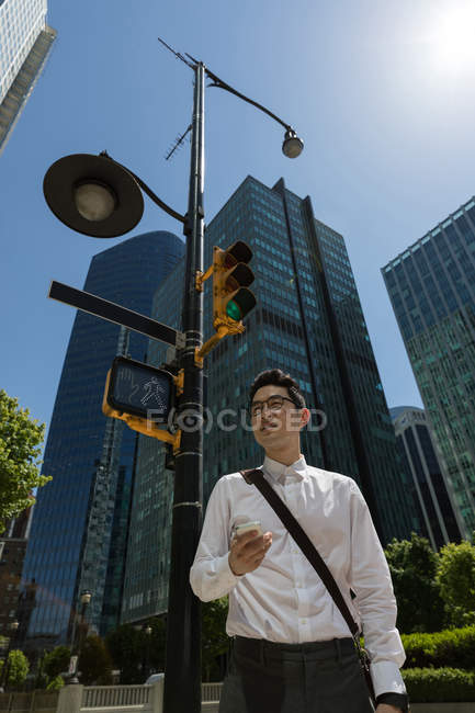 Homme tenant un téléphone portable dans la ville par une journée ensoleillée — Photo de stock